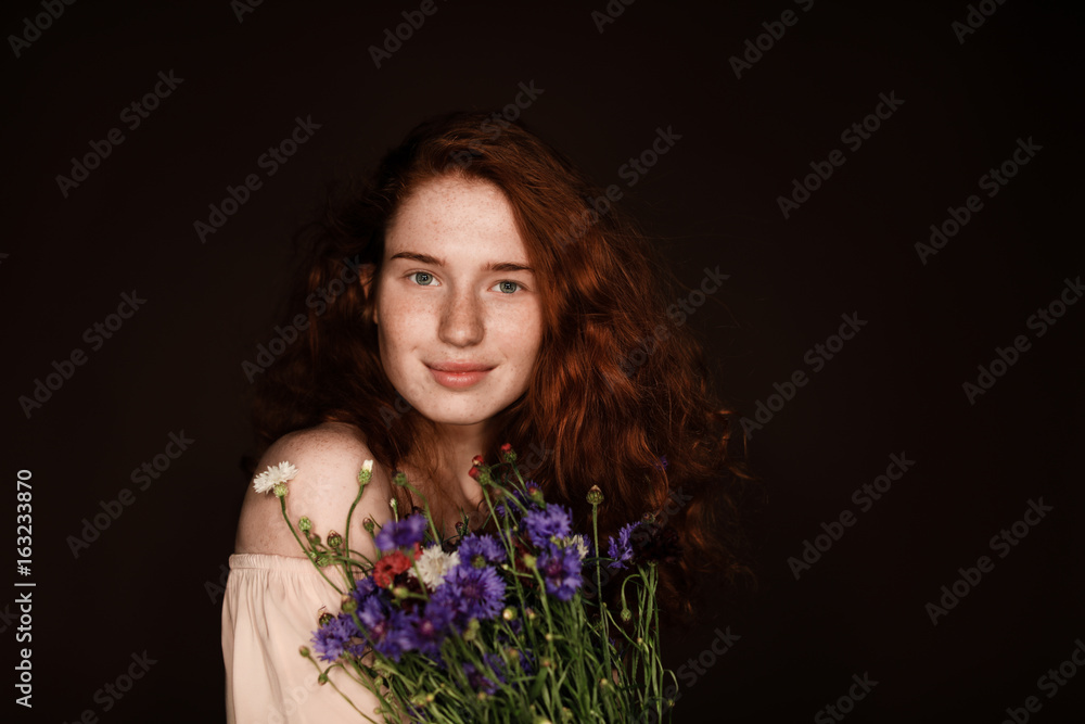 smiling elegant redhead girl holding bouquet of cornflowers, isolated on black with copy space