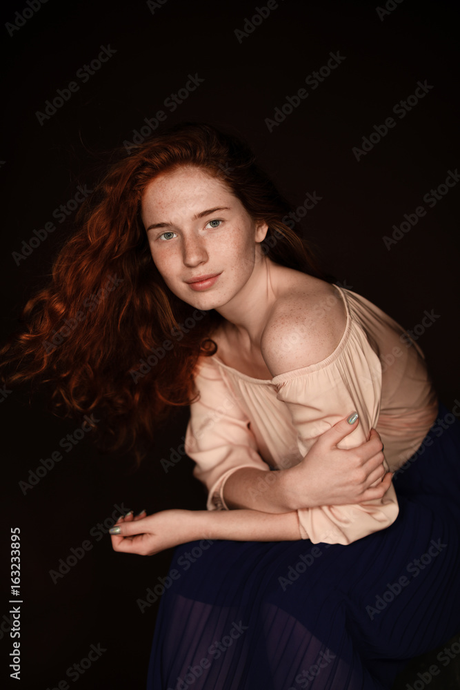 beautiful redhead woman wearing beige blouse looking at camera, isolated on black
