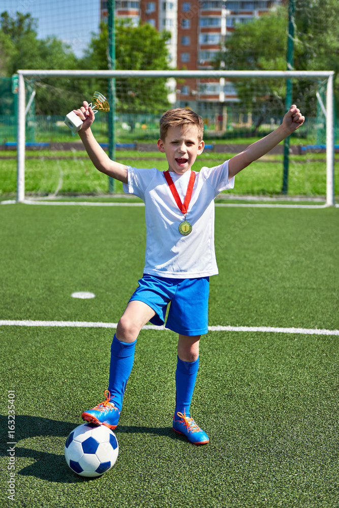 Happy winner boy football player with cup and medal