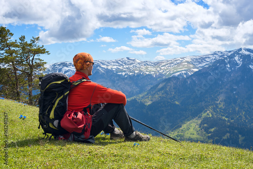 Man adventurer sits on the alpine meadow among the wildflowers