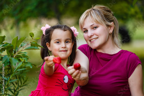 Beautiful little girl and woman  has happy fun smiling face  holding red strawberry. Family portrait. Mom and daughter. People lifestyle. Healthy life.