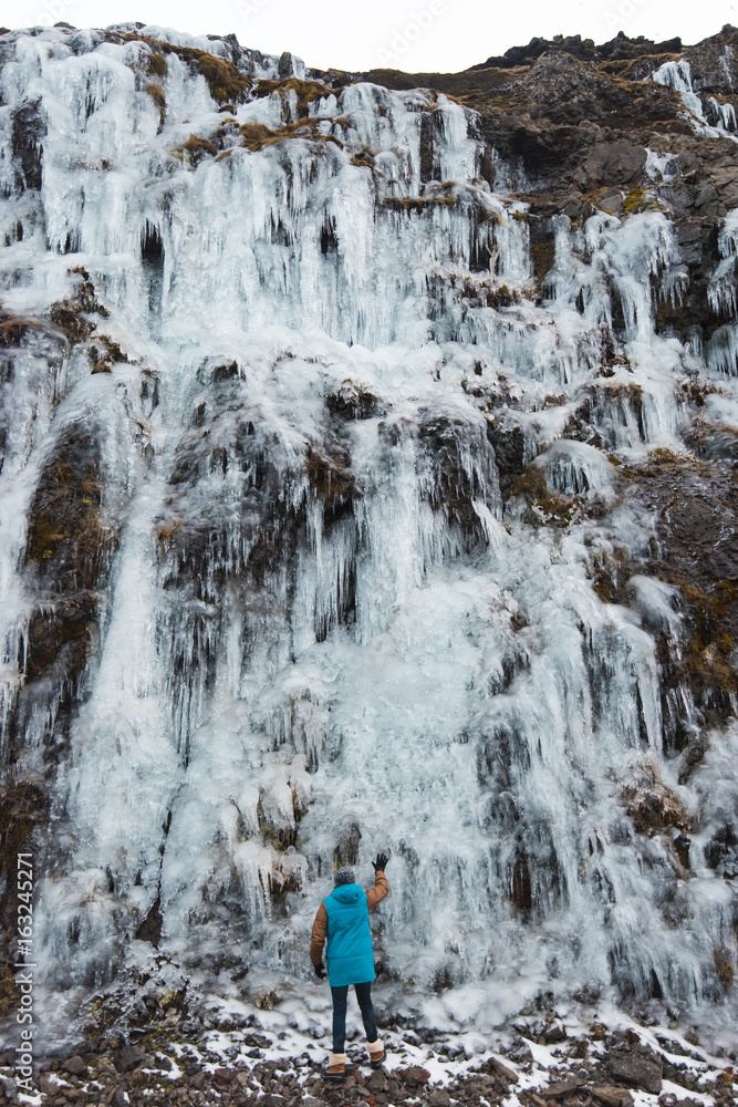 Man standing back to the camera (rear view) by the frozen waterfall, Iceland, Snaefellsnes peninsula Man standing back to the camera (rear view) by the frozen waterfall, Iceland, Snaefellsnes peninsula