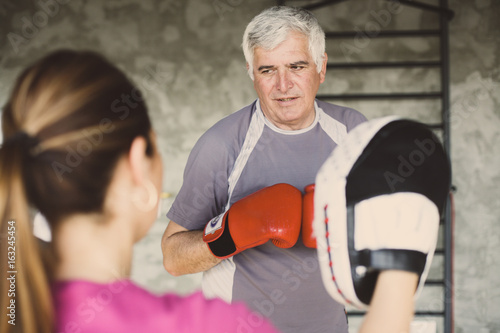 Older man boxing in gym. Senior man with personal trainer.