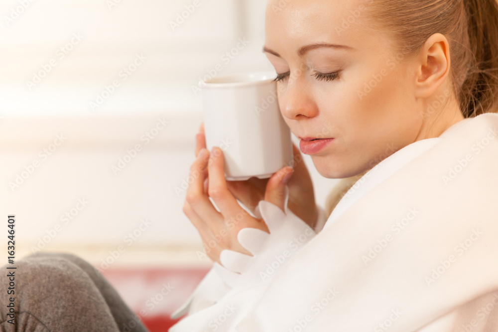 Woman lying on sofa under blanket drinking tea Woman lying on sofa under blanket drinking tea