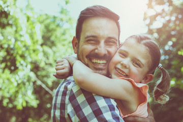 Father holding his daughter in his arms and looking at camera.