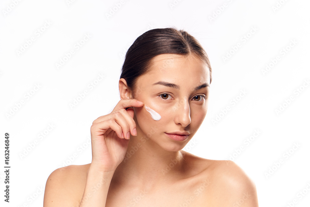 Beautiful young woman on white isolated background applies cosmetic face cream