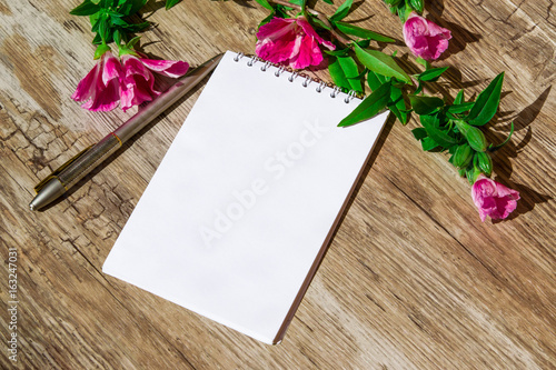 Mocap. Notepad with white paper and pen, decorated with a sprig of pink flowers on a plastic surface, simulated wood, 