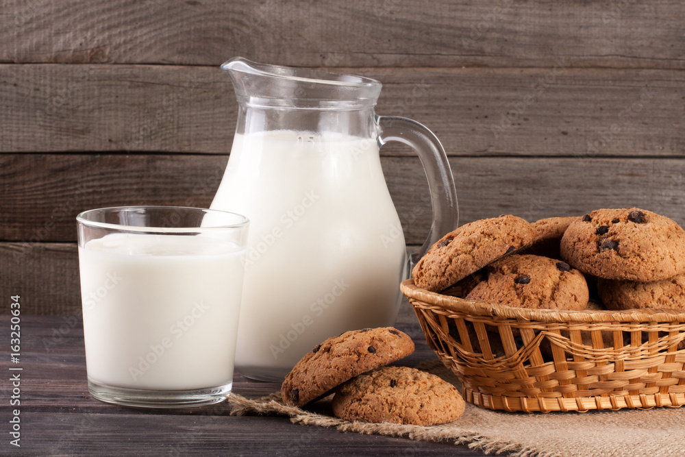 jug and glass of milk with oatmeal cookies in a wicker basket on a wooden background jug and glass of milk with oatmeal cookies in a wicker basket on a wooden background