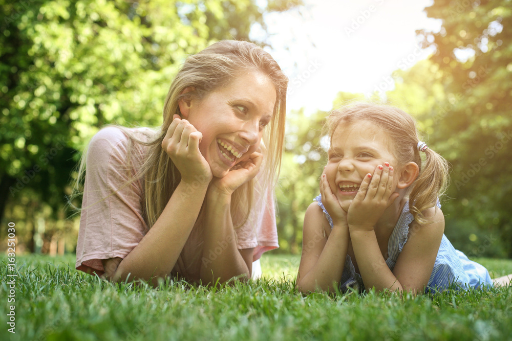 Mother and daughter lying together on green grass. Mother and daughter having funny conversation. Mother and daughter lying together on green grass. Mother and daughter having funny conversation.