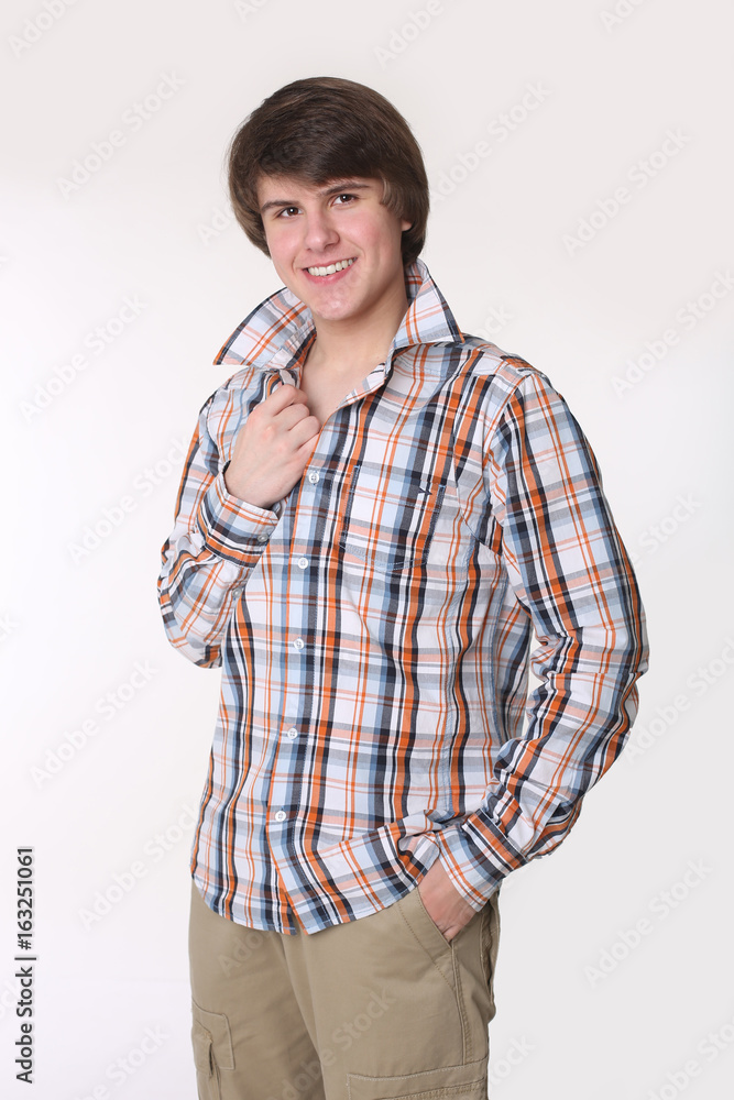 Cheerful toothy young man in checked shirt and smart casual wear looking at camera and holding hands in pockets while standing isolated on studio white background Cheerful toothy young man in checked shirt and smart casual wear looking at camera and holding hands in pockets while standing isolated on studio white background