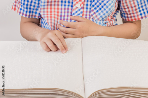 The blind boy is reading a book written on Braille.