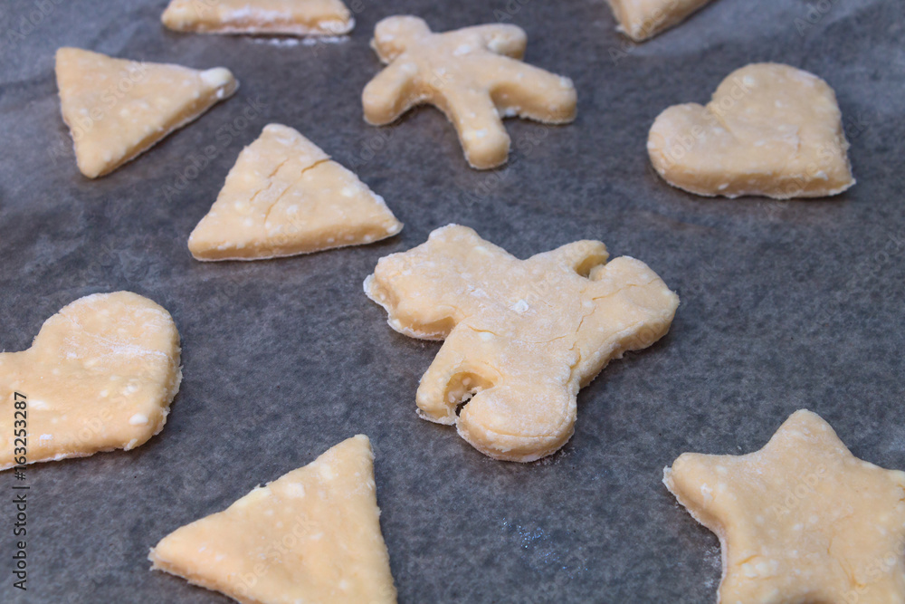 Cookie dough in different shapes lies on the baking sheet.