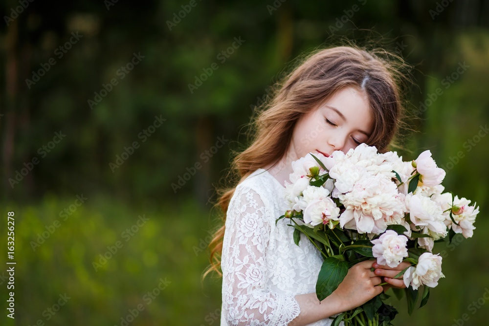 Fototapeta premium little girl six years old with brown hair and blue eyes with a bouquet of peony flowers wearung white dress, smiling