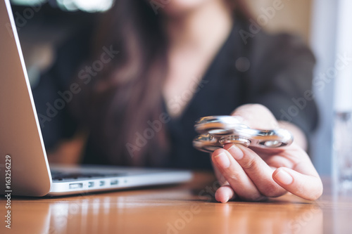 A woman using laptop while playing fidget spinner on wooden table in office