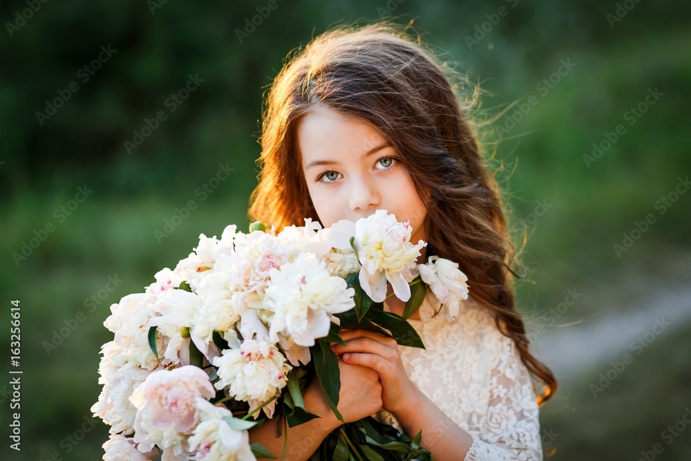 Fototapeta premium little girl six years old with brown hair and blue eyes with a bouquet of peony flowers wearung white dress, smiling