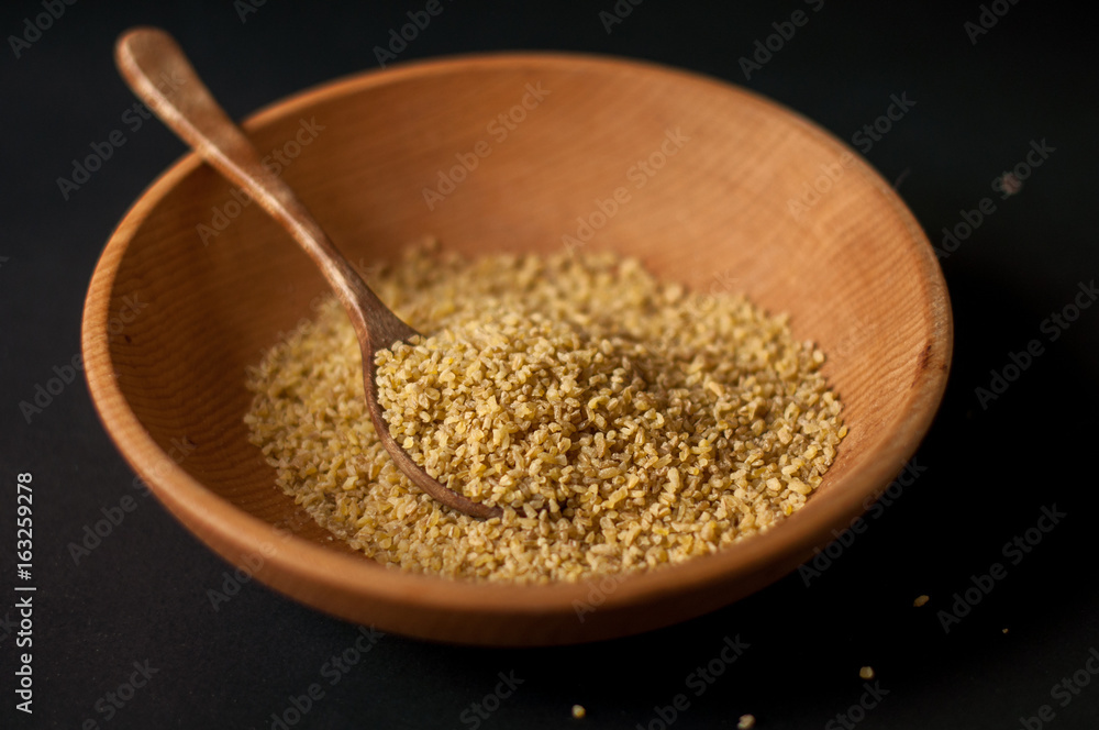 Dry bulgur wheat in brown wooden bowl isolated on dark wood Dry bulgur wheat in brown wooden bowl isolated on dark wood