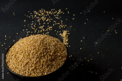 Dry bulgur wheat in brown wooden bowl isolated on dark wood