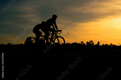 Silhouette of cyclist riding bike on road at sunset.