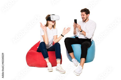 Smiling friends experiencing virtual reality glasses seated on beanbags isolated on white background. photo