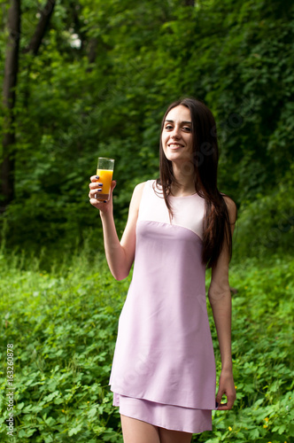 Beautiful slim girl drinks juice from a glass beaker in the park