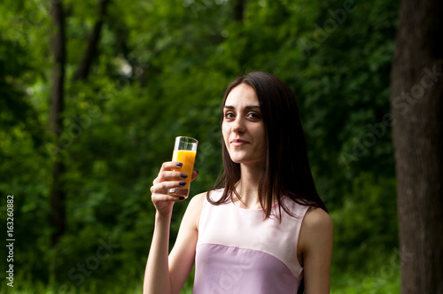 Beautiful slim girl drinks juice from a glass beaker in the park