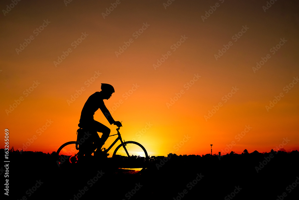 Obraz premium A man rides a bicycle in the evening with orange sky,Silhouette sporty image concept.