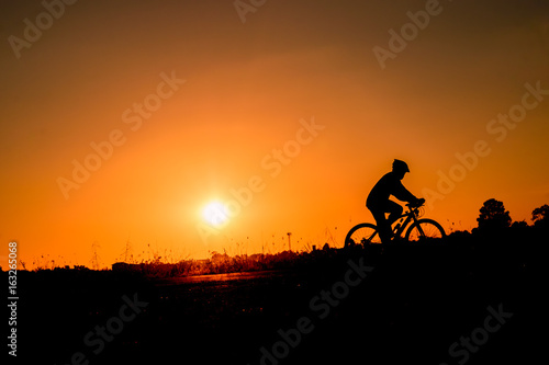 A man rides a bicycle in the evening with orange sky,Silhouette sporty image concept.
