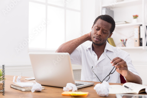 Overworked african-american employee in office, work with laptop