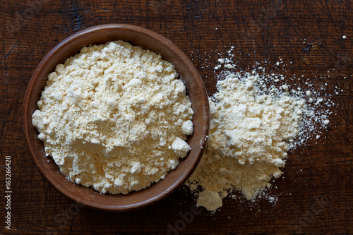 Chickpea flour in dark wooden bowl isolated on dark brown wood from above. Spilled flour. photo