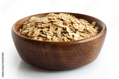 Dry whole porridge oats in dark wooden bowl isolated on white.