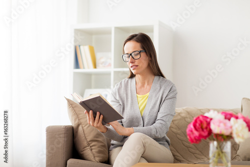 young woman in glasses reading book at home