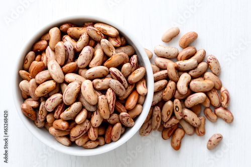 Obraz na plátně Dry pinto beans in white ceramic bowl isolated on painted white wood from above