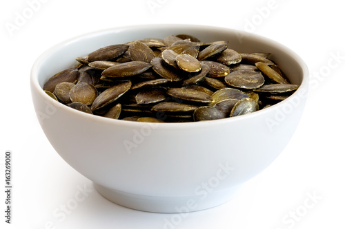 Hulled pumpkin seeds in white ceramic bowl isolated on white.