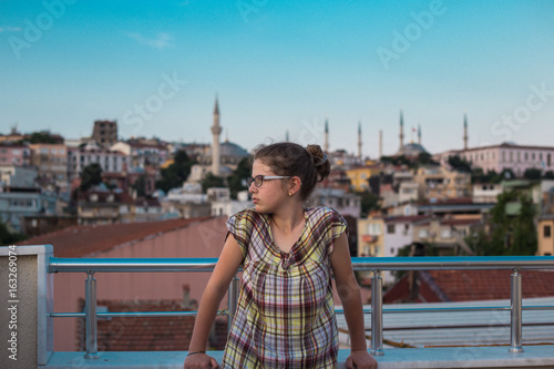 Young blue girl standing on the terrace, view of the panorama of the city, view of the distance, sunset © HappyLenses
