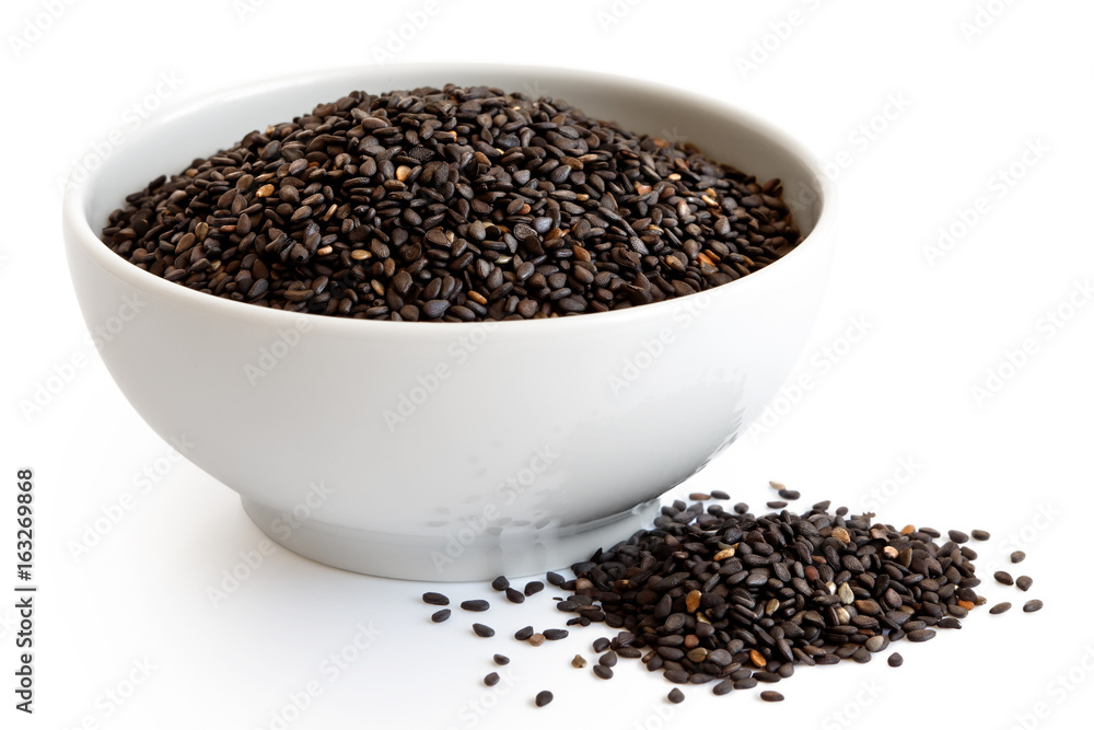 Black sesame seeds in white ceranic bowl isolated on white. Spilled seeds. Black sesame seeds in white ceranic bowl isolated on white. Spilled seeds.