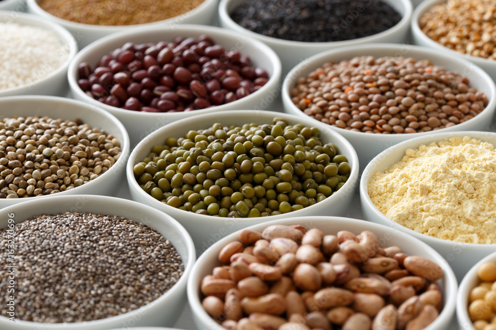 Arranged white bowls with uncooked pulses, grains and seeds on white wood. Arranged white bowls with uncooked pulses, grains and seeds on white wood.