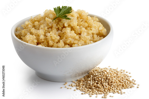 Cooked quinoa in white ceramic bowl isolated on white with green parsley. Spilled uncooked quinoa. photo