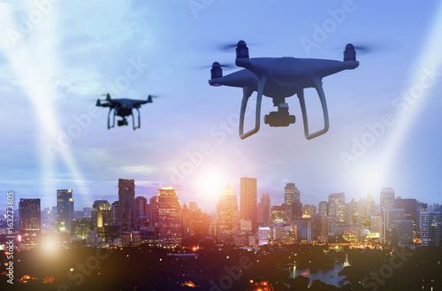 Drones (Multi-rotor) silhouette flying above the city panorama at night scene to find something with spotlight.