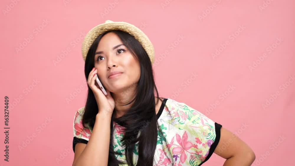 Young happy asian woman wearing hat talking by phone over pink background Young happy asian woman wearing hat talking by phone over pink background