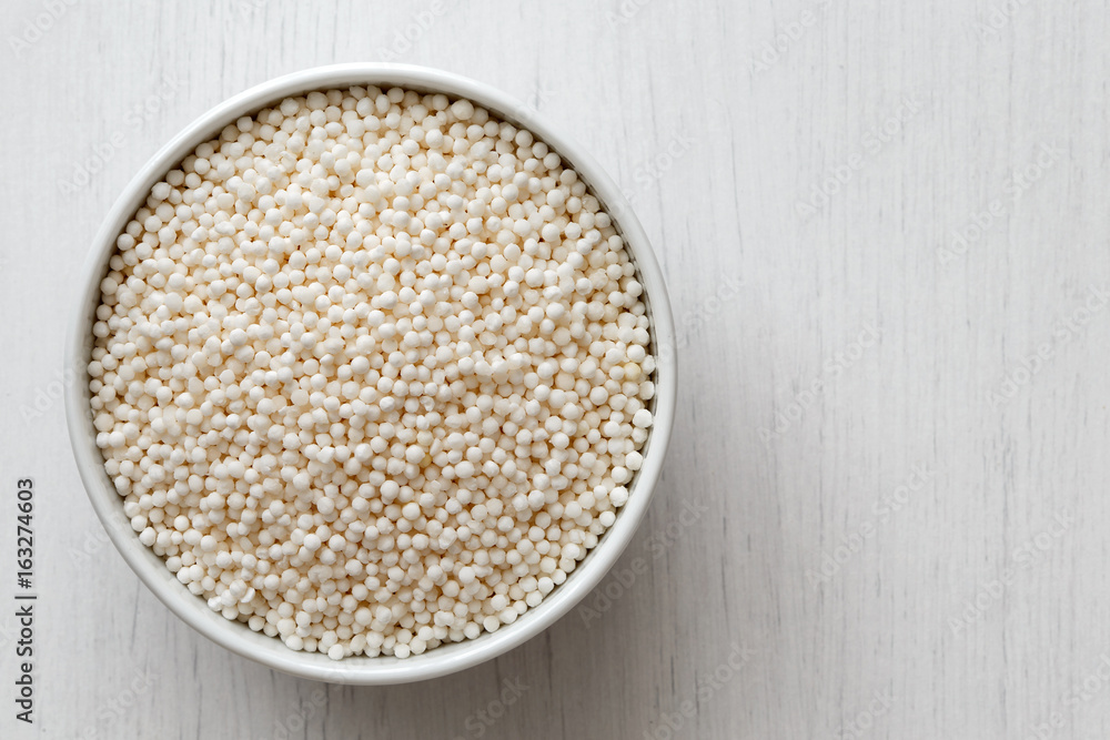 Dry tapioca pearls in white ceramic dish isolated on painted white wood from above. Dry tapioca pearls in white ceramic dish isolated on painted white wood from above.