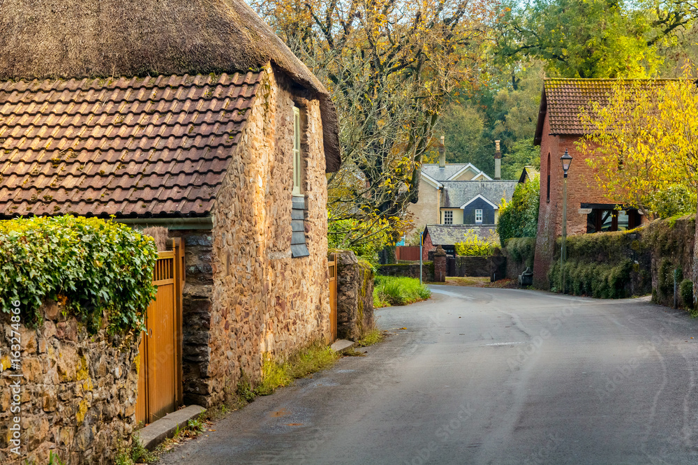 A quiet street with old houses in the village of Cockington. Autumn warm day. Foliage flies from trees. Devon. England