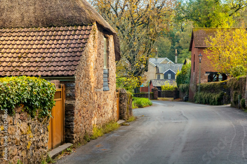 A quiet street with old houses in the village of Cockington. Autumn warm day. Foliage flies from trees. Devon. England