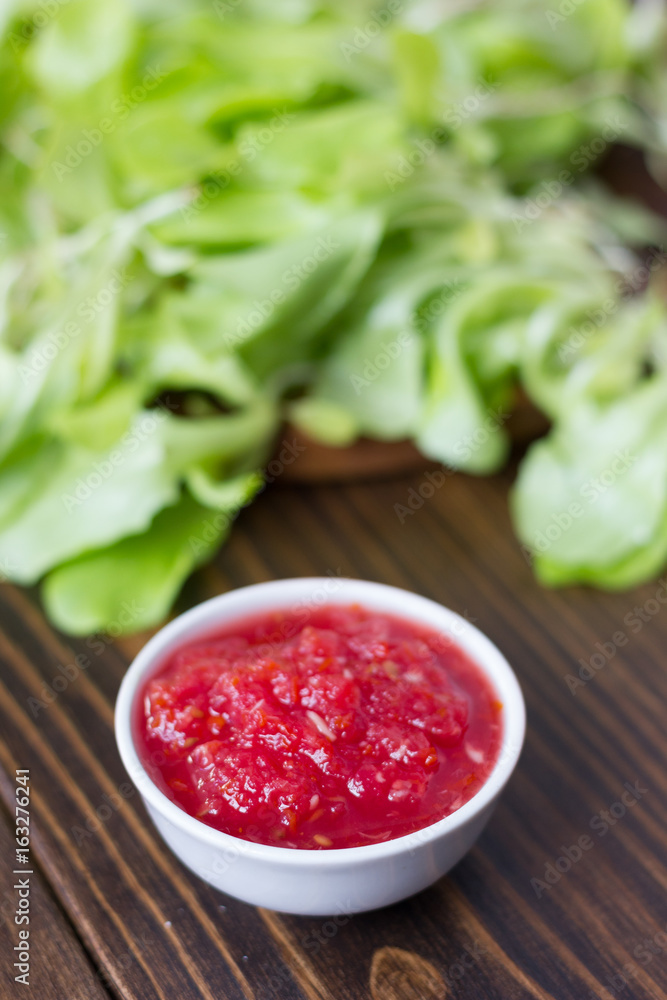 Mexican salsa or indian chutney in white ceramic bowl against green herbs