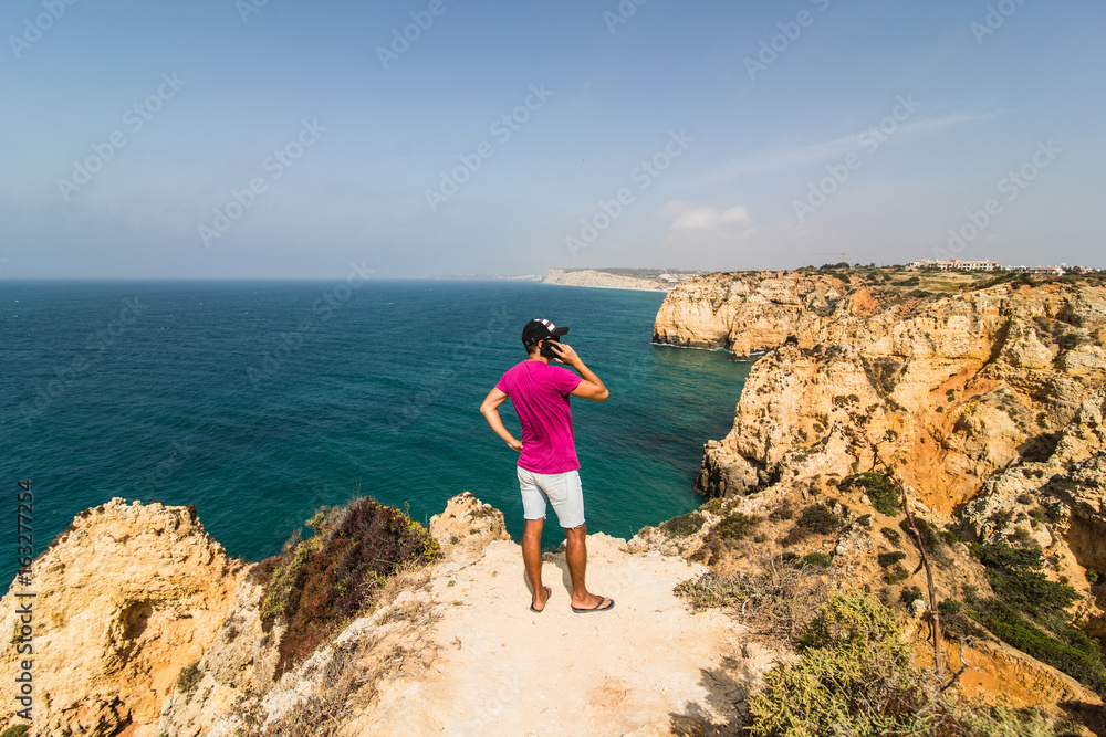 Man in end of the rock near atlantic ocean speak on phone on  summer sunny days