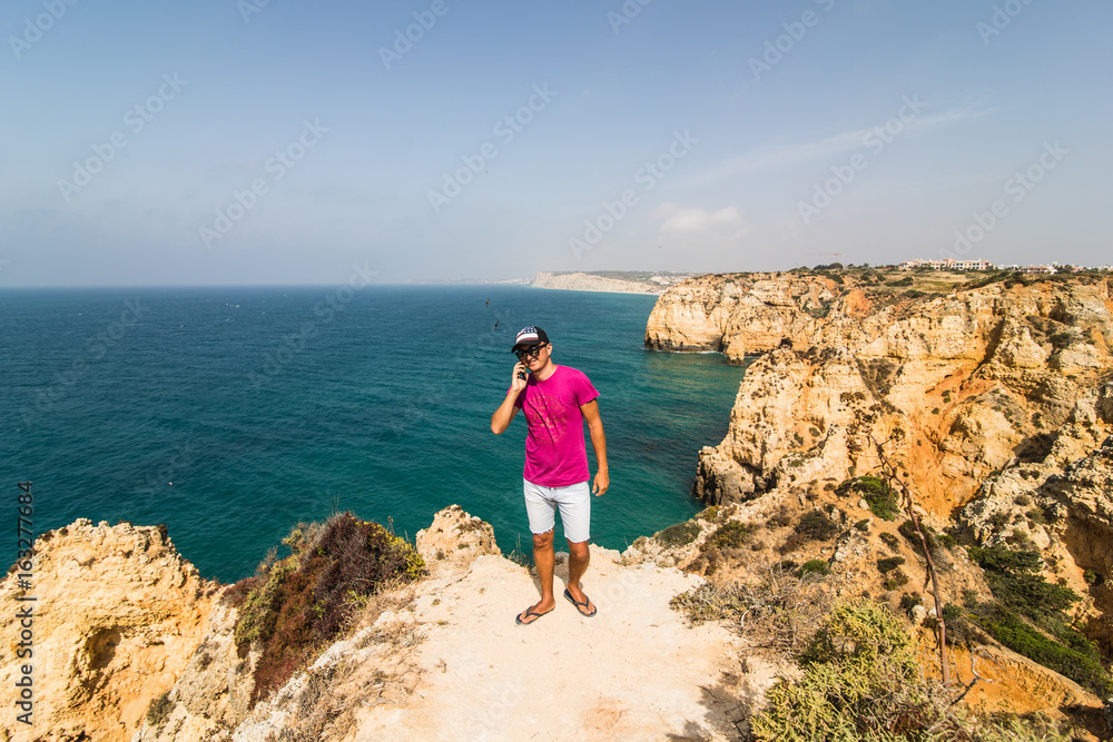 Man in end of the rock near atlantic ocean speak on phone on summer sunny days Man in end of the rock near atlantic ocean speak on phone on summer sunny days