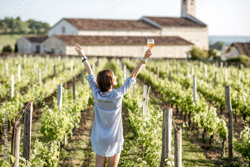 Wall Mural Young woman with glass of wine enjoying beautiful sunset view on the vineyard in
