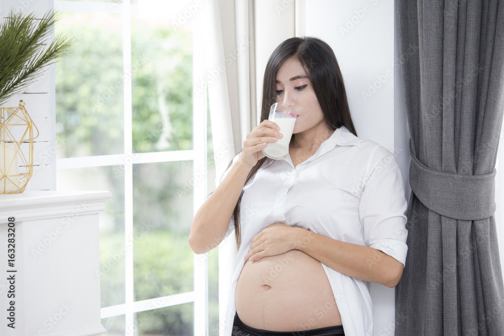 Young asian pregnant woman drinking milk and showing her belly and carefully holding. Young asian pregnant woman drinking milk and showing her belly and carefully holding.