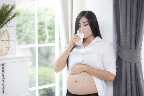 Young asian pregnant woman drinking milk and showing her belly and carefully holding.