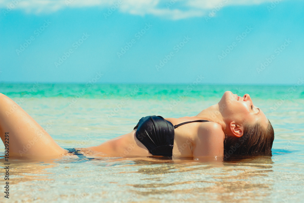 Young beautiful girl lies in the sea on the beach, it is washed by waves, she closed her eyes from appeasement Young beautiful girl lies in the sea on the beach, it is washed by waves, she closed her eyes from appeasement