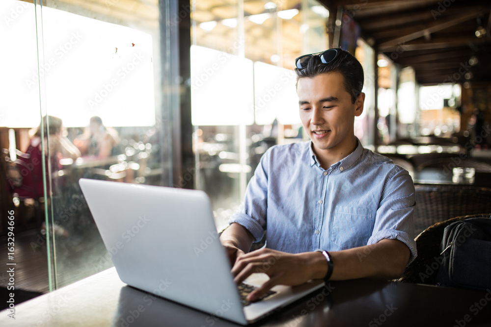 Portrait of handsome asian smiling man using laptop in the cafe Portrait of handsome asian smiling man using laptop in the cafe